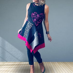 May include: A sleeveless tunic featuring a dark gray base with a large pink floral heart graphic on the chest. The garment has an asymmetrical hem with patchwork panels in black, white, and gray patterns, accented by pink cross-stitch embroidery.