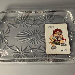 May include: A clear glass serving tray with a starburst pattern. A playing card with a cartoon joker character is on the tray. The card reads "JOKER" at the top and bottom.