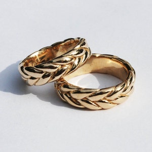 May include: Two gold braided wedding bands. The bands are thick and have a rope-like design.