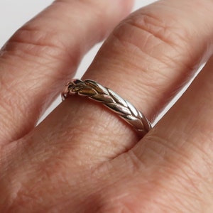 Puede incluir: Un anillo trenzado de plata y oro usado en un dedo.