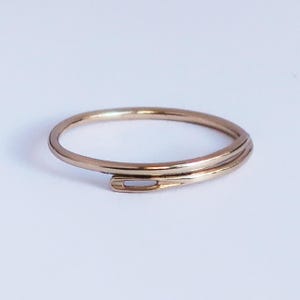 May include: A delicate gold-coloured ring with a spiral design. The ring appears to be made of a thin, continuous band of metal, wrapping around to form a unique shape. The ring is set against a plain white background.
