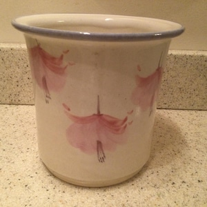 May include: White ceramic utensil holder with a blue rim and pink floral designs.