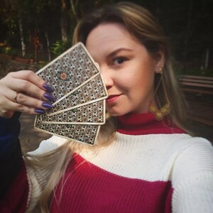 May include: A woman holds a fan of playing cards in front of her face. The cards have a patterned design with a black and white color scheme. The woman is wearing a red and white striped sweater.