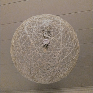 Può includere: Un paralume bianco rotondo e intrecciato appeso al soffitto. Il paralume è realizzato con un delicato e intricato motivo di fili intrecciati.