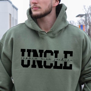 May include: A green hooded sweatshirt with the word "UNCLE" printed in large black letters. The names "sophia anna jackson" are written in cursive script below the word "UNCLE".