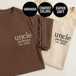 May include: Two t-shirts, one brown and one beige, with the text "uncle jackson est. 2025" embroidered on the front. The shirts are made of soft, comfortable fabric and are perfect for everyday wear.
