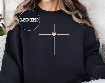 May include: A navy blue sweatshirt with a beige cross design and a heart in the center. The word "EMBROIDERED" is in a circle on the upper left. The sweatshirt is a comfortable, casual top.
