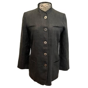 May include: A dark gray blazer with a mandarin collar and four buttons. The blazer has two front pockets and two small chest pockets. The sleeves are long and the fabric appears to be linen or a linen blend.