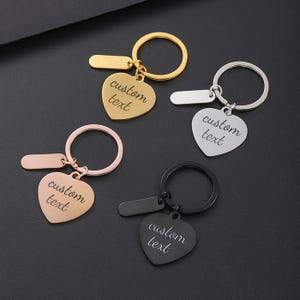 May include: Four heart-shaped keychains with different colored metal finishes. Each keychain has a ring and a small tag that says "custom text".