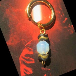 Peut inclure: Une boucle d'oreille en or avec une pierre d'opale blanche et des perles noires et dorées qui pendent.