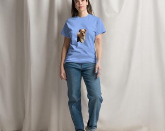 Può includere: Una t-shirt blu chiaro con una grafica di un piccolo cane che spunta da un buco. La persona che indossa la t-shirt è in piedi davanti a uno sfondo bianco.