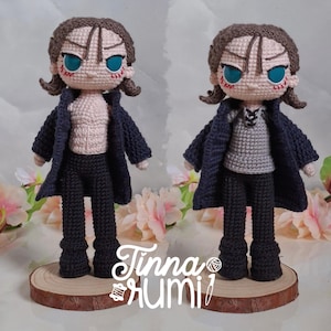 Puede incluir: Dos muñecos de ganchillo hechos a mano, cada uno con cabello castaño, ojos azules y un abrigo azul oscuro. Uno de los muñecos está sin camisa, el otro lleva una camisa gris. Están sobre rodajas de madera. Los muñecos son un artículo artesanal.