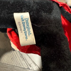 May include: A black plush toy with a red polka dot bow and a yellow accent. The tag reads "Disneyland Walt Disney World &copy;Disney".