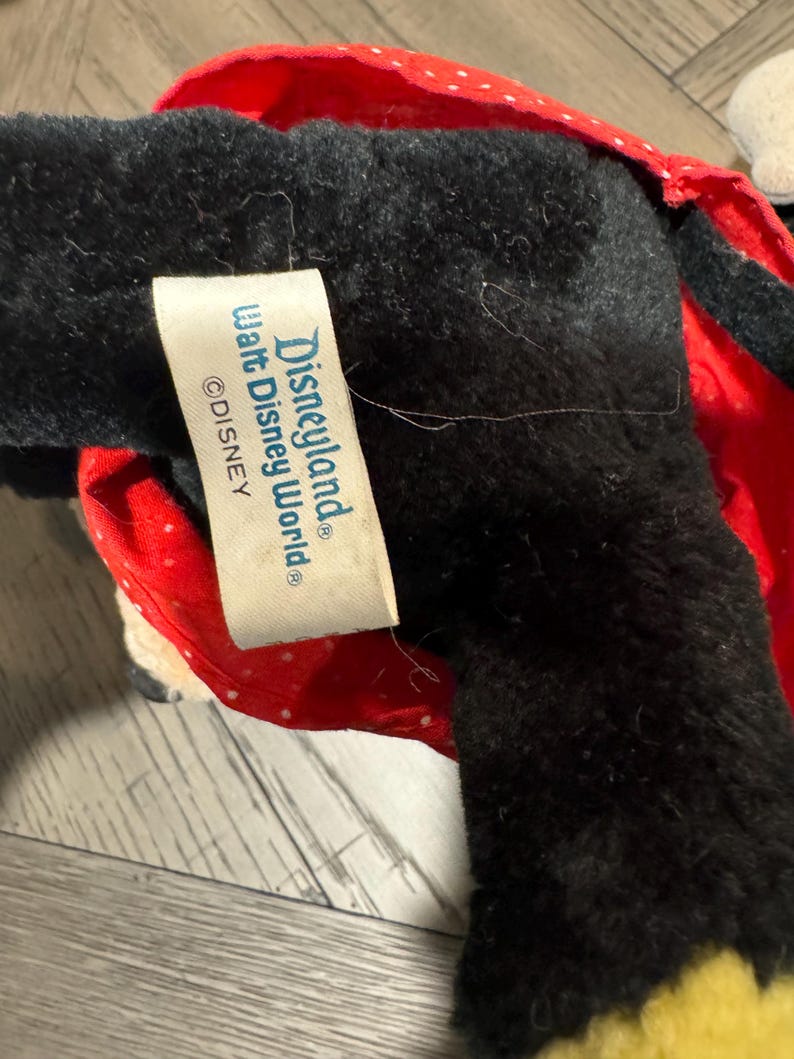 May include: A black plush toy with a red polka dot bow and a yellow accent. The tag reads "Disneyland Walt Disney World &copy;Disney".