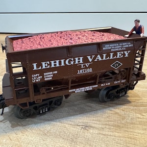 May include: A brown model train car from the Lehigh Valley, LV 167103, filled with pink material. The text on the side reads "ORE SERVICE - NJ INC CO. RETURN TO AGENT - LAHR BBY FRANKLIN, N.J." and "HOPPER CAR DOORS MUST BE CLOSED BEFORE CAR IS MOVED."