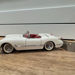 May include: A white classic convertible car model with red interior. The model has chrome accents, white-wall tires, and a clear windshield. The car is a vintage style, likely a collectible item.