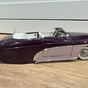 May include: A vintage-style convertible car model in a two-tone color scheme. The front and rear sections are a deep burgundy, while the middle section is a light mauve. The car has white-walled tires and chrome accents, giving it a classic look.