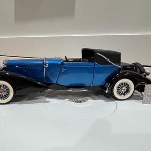 May include: A blue and black vintage convertible car model with white-walled tires. The model has a black convertible top and chrome accents. The car is a detailed replica of a classic automobile.