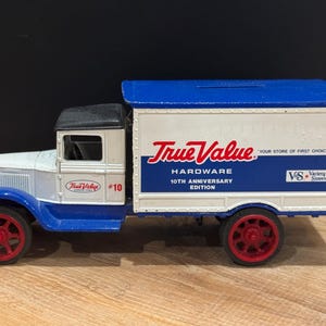 May include: A die-cast True Value Hardware truck, featuring a white body with blue and red accents. The truck has the True Value logo and "10th Anniversary Edition" text. The wheels are red.