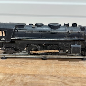 May include: A black model train, featuring the number 666, sits on a track. The vintage engine has detailed wheels and mechanical components. A classic toy train, reminiscent of a bygone era.