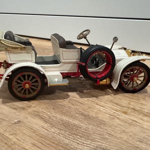 May include: A white ceramic mug with a black handle and the text "But First, Coffee" in a bold, black font. The mug is on a wooden surface. The mug is approximately 10 cm tall.