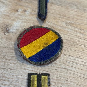 Puede incluir: Tres parches militares vintage. Un parche redondo con rayas rojas, amarillas y azules. Un parche verde y negro con un extremo puntiagudo. Un parche negro con dos rayas doradas.