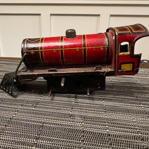 Könnte beinhalten: Vintage Spielzeug-Zug in Rot mit schwarzen und goldenen Akzenten. Der Metallzug hat einen Schornstein, Fenster und einen Kuhfänger. Ein klassisches Sammlerstück mit detailliertem Design. Ein nostalgisches Stück.