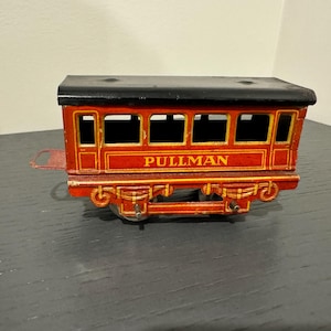May include: A red and black toy train car with the word "PULLMAN" printed on the side. The car has windows and a black roof.