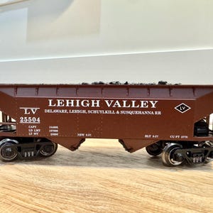 May include: A brown model train car with the text "LEHIGH VALLEY" and "DELAWARE, LEHIGH, SCHUYLKILL & SUSQUEHANNA RR". The car has the number 25504 and is filled with a dark material.