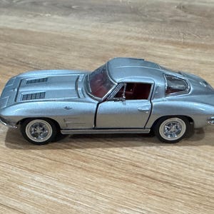 Op de afbeelding: Zilveren modelauto met een rood interieur. De klassieke sportwagen heeft een strak design, gedetailleerde wielen en een laag profiel. Het model wordt gepresenteerd op een houten oppervlak.