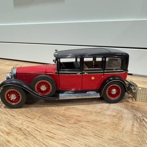 Peut inclure: Modèle de voiture ancienne rouge et noire avec des ailes noires et un toit noir. La voiture a des roues rouges avec un centre doré et des accents argentés. Le modèle est une réplique détaillée d'une automobile classique.