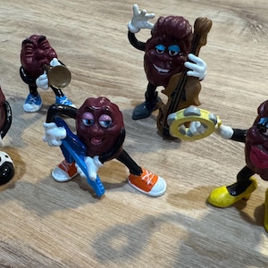 The California Raisins Toy Figures -1987 Sax the Raisin Figure- 1988 Trumpy True Note- 1988 Mrs. Marvelous-  1988 Cello Player- 1988 Guitar