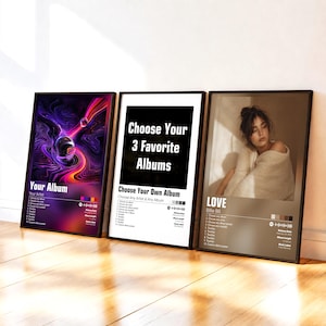 May include: Three rectangular framed posters displayed side-by-side. The left poster features a purple and orange abstract sphere design. The center poster has a white background with black text reading Choose Your 3 Favorite Albums. The right poster displays a photographic portrait of a person with brown hair, titled LOVE by Billie Bili, with track lists and Spotify-style codes.