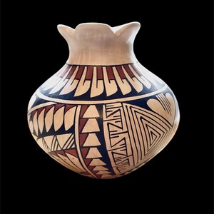 May include: A white ceramic pot with a geometric design in black, red, and brown. The pot has a wide mouth and a rounded body.