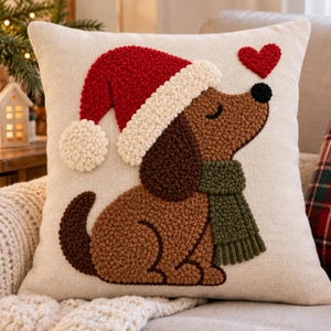 May include: A square off-white throw pillow featuring a textured punch needle design of a brown dog wearing a red Santa hat with a white pom-pom and a green scarf. A small red heart is positioned above the dog's nose on the cream-colored fabric.