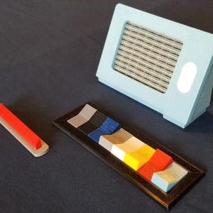 May include: A set of colorful plastic pieces in a black frame, a light blue box with a speaker grille, and a red plastic piece on a silver base.