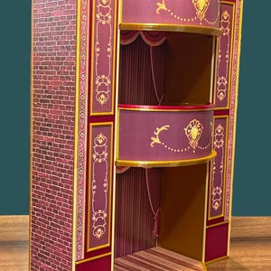 May include: A miniature theatre stage with a brick wall on the left. The stage has two levels with burgundy and gold accents, and a curved front. The stage is decorated with gold embellishments and curtains.