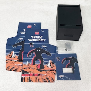 Puede incluir: Tres superposiciones de panel de control de gabinete de arcade azul y naranja con un gráfico de monstruo invasor espacial y el texto "Space Invaders".