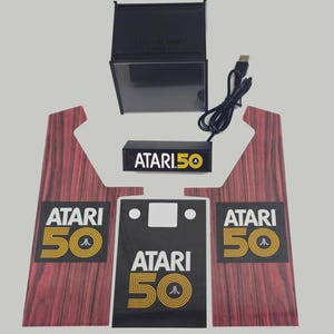 May include: A black and yellow Atari 50th Anniversary logo on a black background. The logo is surrounded by a red woodgrain border. The logo is part of a set of stickers for a custom arcade cabinet.