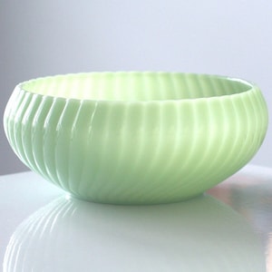 May include: A light green, oval-shaped bowl with a ribbed exterior. The bowl has a smooth, glossy finish and reflects light. The bowl is likely made of glass or a similar material. The bowl is a decorative item.