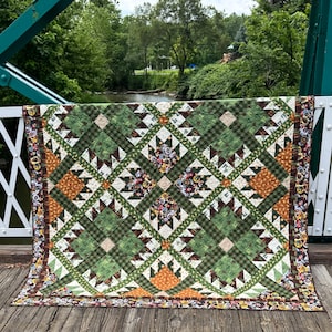 May include: A rectangular quilt featuring a geometric pattern of green, brown, and orange fabric squares. The design includes repeating star-like shapes and a border decorated with small circular motifs in various colors, including red and yellow.
