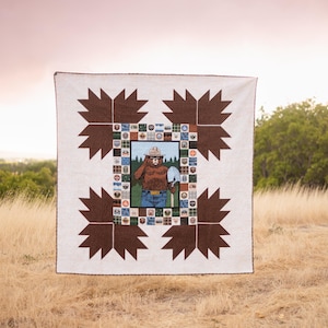 Pode incluir: Um edredom branco com um design de estrela marrom. O centro do edredom apresenta uma imagem de um urso usando um chapéu de guarda florestal e segurando uma pá. O urso é cercado por uma borda de quadrados pequenos com diferentes imagens.