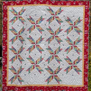 May include: A white quilt with a repeating pattern of colorful pinwheels. The quilt is edged with a red and white floral fabric.