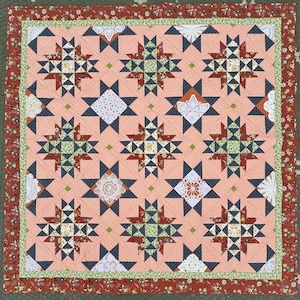 May include: A handmade quilt with a peach-colored background and a repeating star pattern. The stars are composed of navy blue, rust, and green fabrics. The quilt is bordered with floral and green patterned fabric.