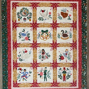 May include: A Christmas-themed quilt with twelve embroidered squares, each depicting a verse from the "Twelve Days of Christmas" carol. The quilt features a red and gold patterned background, with a green border.