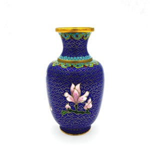 Op de afbeelding: Een blauwe cloisonné vaas met een bloemenontwerp. De vaas heeft een gouden rand en voet, met een gedetailleerd wolkenpatroon en een roze bloem met groene bladeren. De vaas is ongeveer 15 cm hoog.