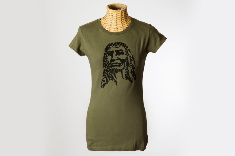 May include: A green t-shirt with a black graphic print of a person's face. The graphic is made up of words, including "The Earth is our", "We believe", and "Care for the Earth".