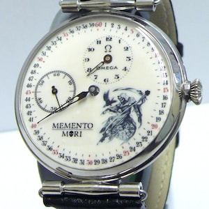 May include: A silver-toned wristwatch with a black leather strap and a white dial. The dial features a central Omega logo, a sub-dial, a grim reaper illustration, and the text MEMENTO MORI. A numbered scale from 1 to 60 circles the dial edge.
