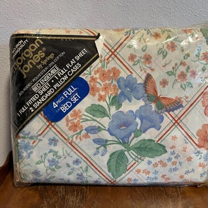May include: A 4-piece full bed set in a plastic package. The sheets feature a floral pattern with blue and peach flowers, green leaves, and a butterfly. The packaging includes the brand name "Morgan Jones" and the words "Bed Ensemble".