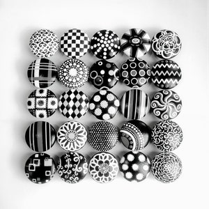May include: A set of 25 black and white painted round knobs with various geometric and abstract designs.